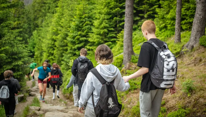 Eine Gruppe Jugendlicher wandert einen steinigen Weg durch den Fichtenwald