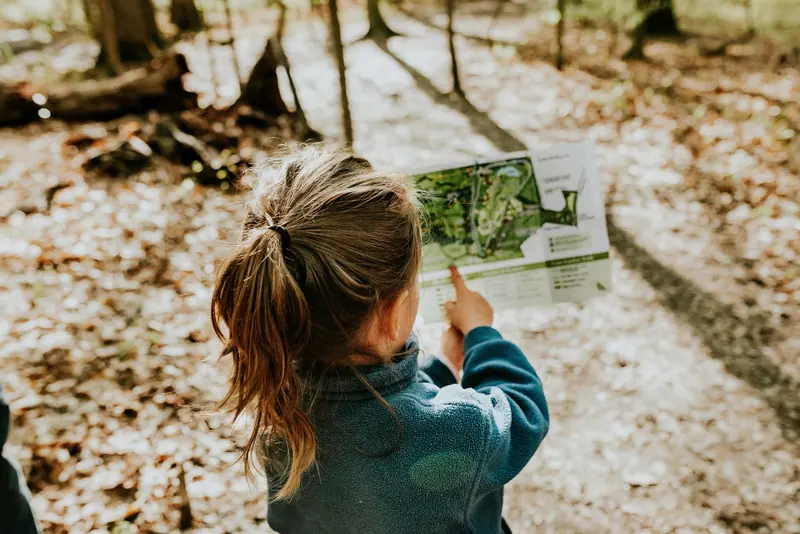 Ein Mädchen zeigt im Wald auf eine Wanderkarte, die sie in den Händen hält